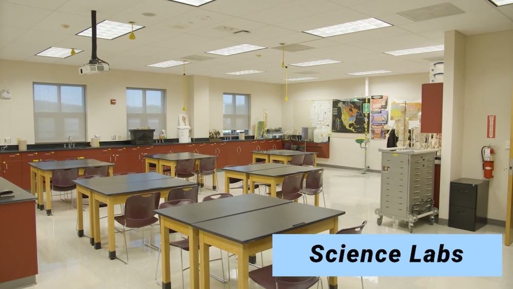 Photo of science lab showing empty desks and a counter with sinks lining the far wall.