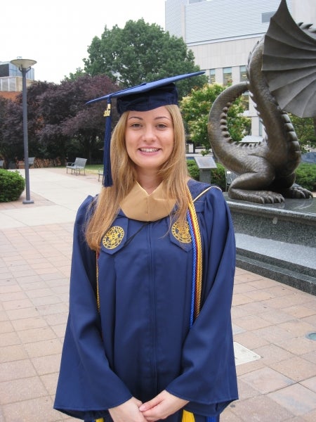 Irena in graduation attire standing in front of a statue of the Drexel dragon.