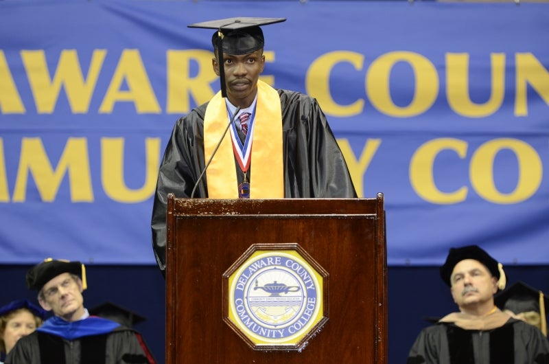 Isaac in graduation attire giving a speech at a podium.