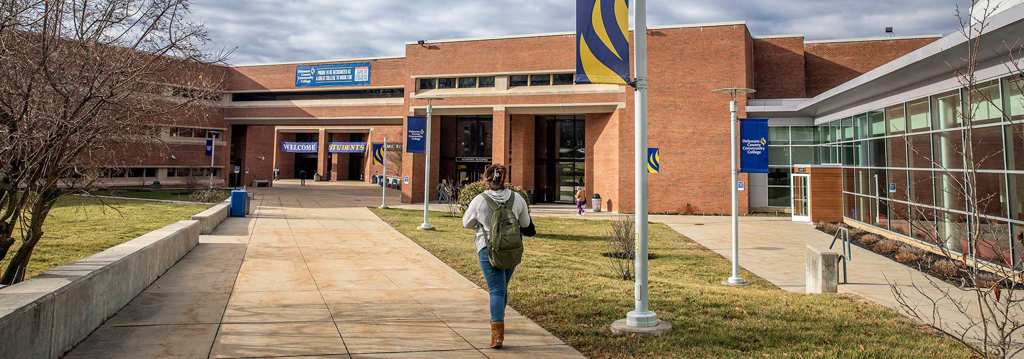 A student walking toward the entrance of Delaware County Community College’s Academic Building on a sunny day.