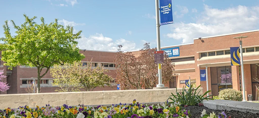 A view of Delaware County Community College campus with trees, flowers, and banners showcasing the college’s branding.