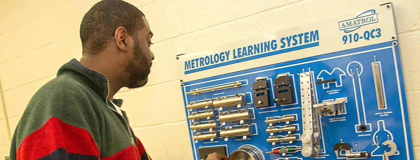 A student examining a metrology learning system display, featuring precision measurement tools and components.