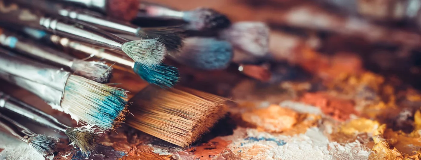 Close-up of colorful paintbrushes with dried paint on a vibrant painter's palette.