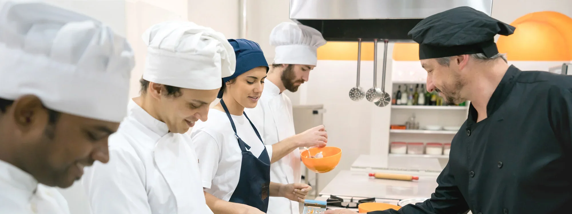 A group of culinary students working under the guidance of a chef in a professional kitchen environment."