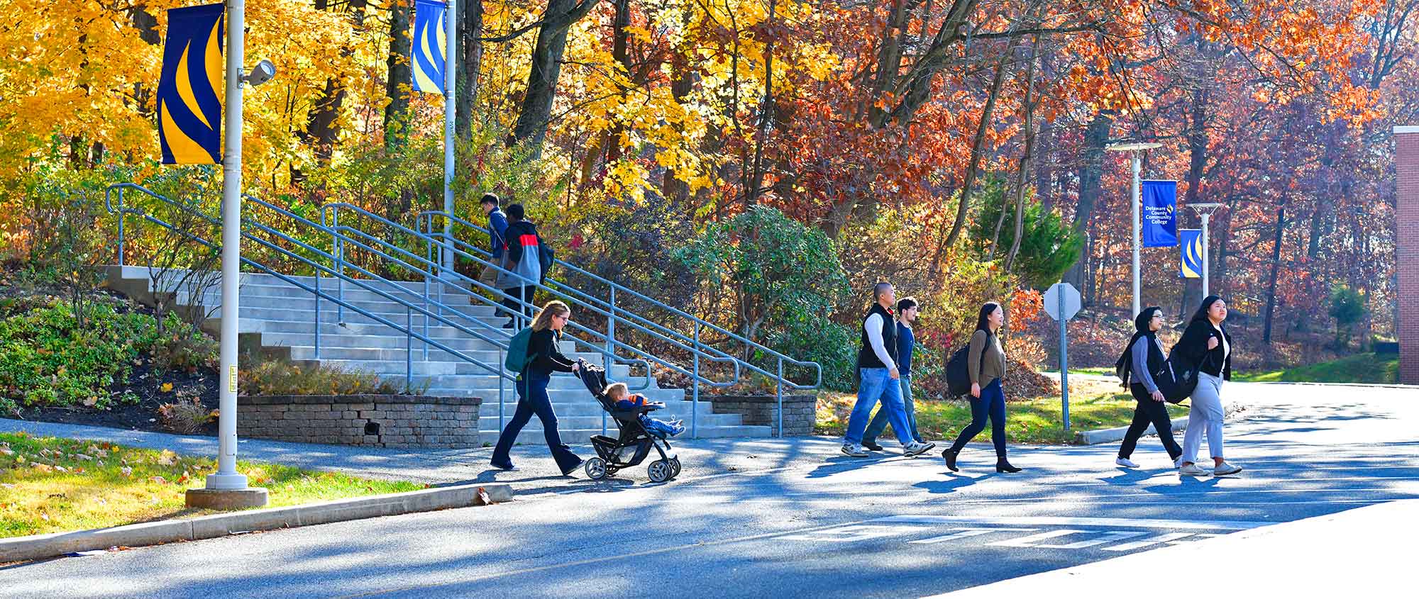 Students walking on campus during autumn, surrounded by vibrant fall foliage and Delaware County Community College banners in the background.