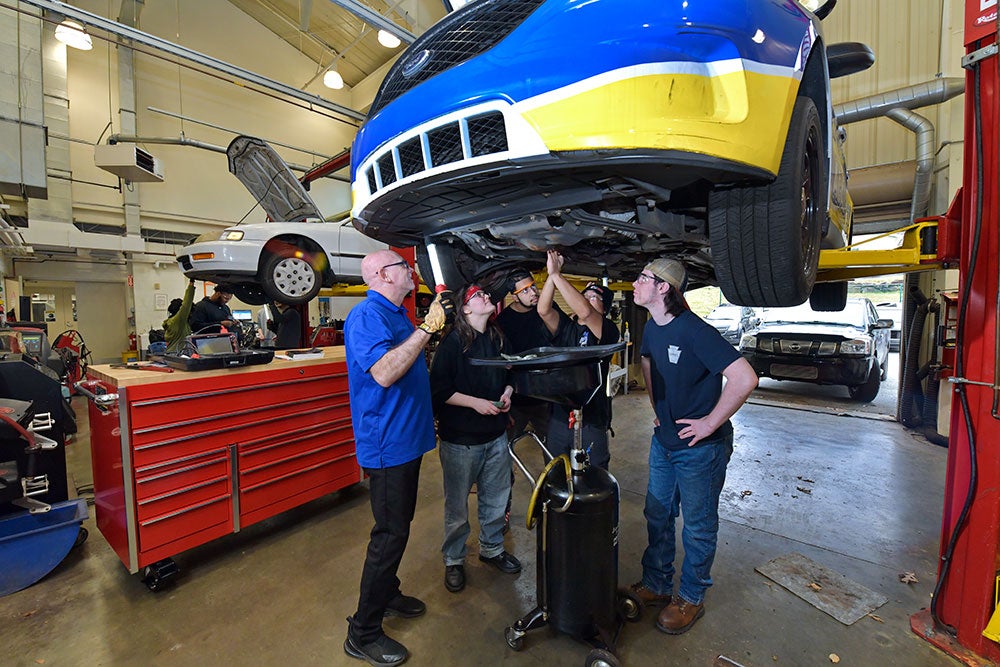 Automotive instructor with students standing under elevated vehicle