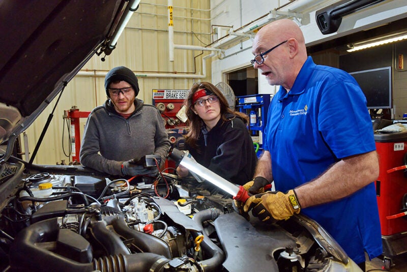Automotive instructor with students looking under hood of car