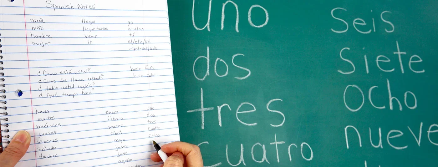 A notebook with Spanish vocabulary and grammar notes alongside a chalkboard displaying numbers in Spanish from uno to nueve.
