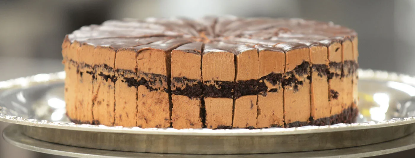 A rich chocolate layer cake with smooth frosting and dark chocolate layers, placed on an elegant silver platter."