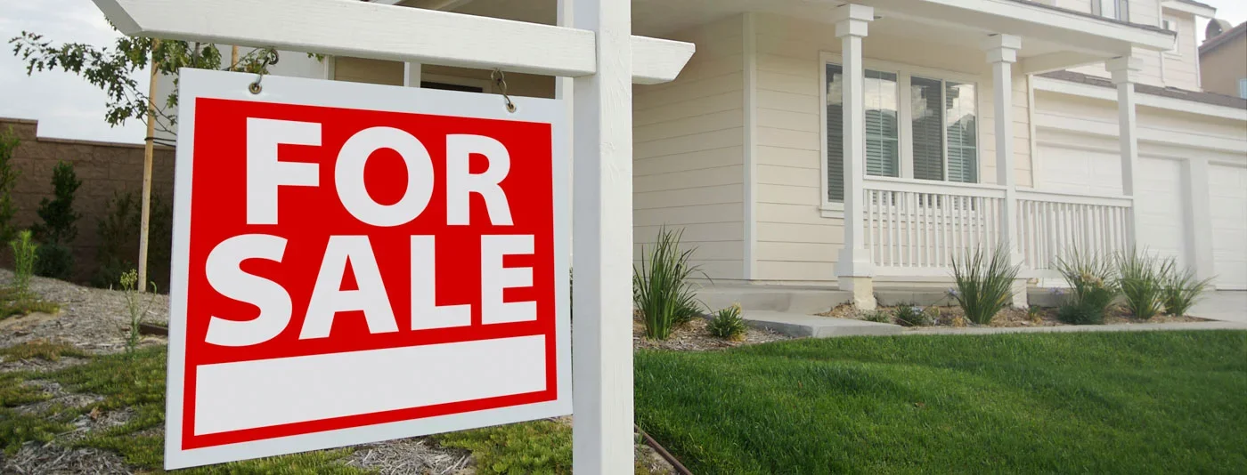 A red and white ‘For Sale’ sign in front of a modern suburban house with a well-maintained lawn and porch