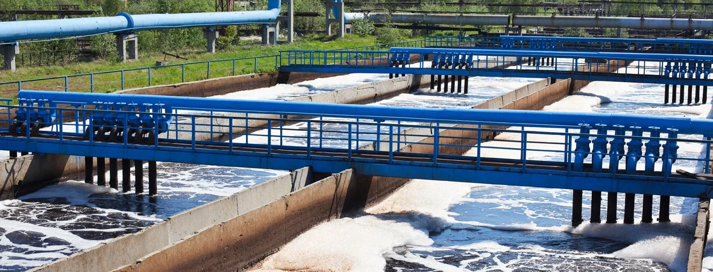 A wastewater treatment facility with multiple aeration tanks and blue piping systems, processing water in an industrial setting