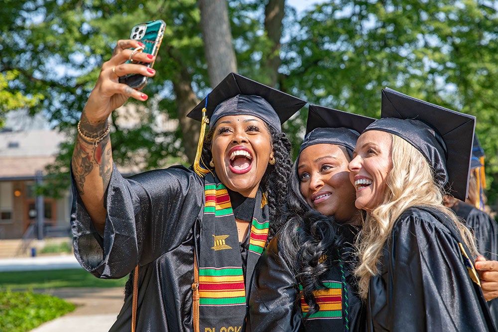 three women wearing caps and gowns, smiling for a selfie