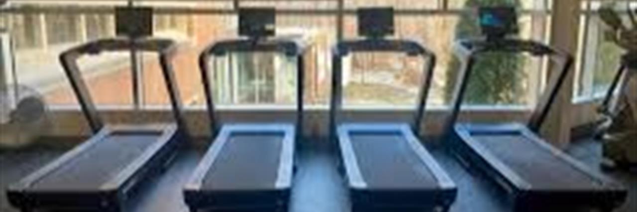 Four treadmills lined up in front of windows