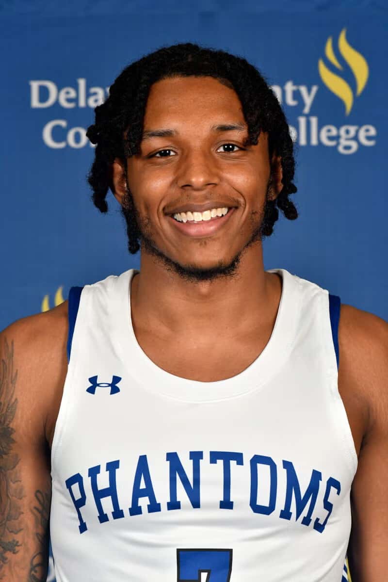 Smiling basketball player in a Phantoms jersey posing in front of a Delaware County Community College backdrop.