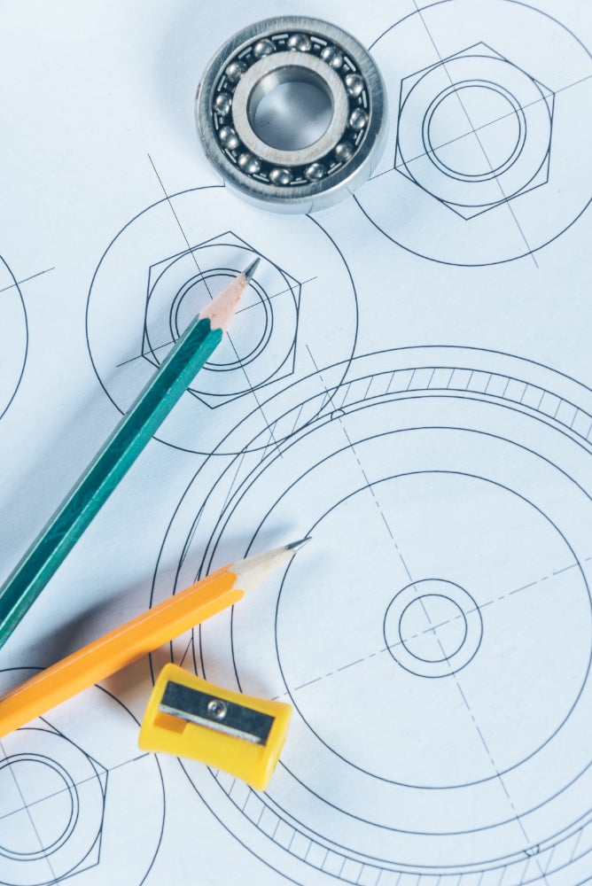 Close-up of technical drawings with geometric shapes, a bearing, and two pencils with a sharpener, symbolizing engineering and design work.