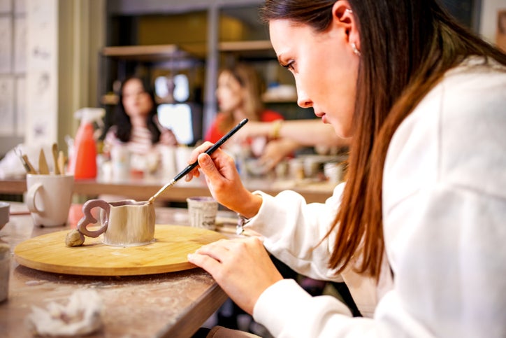 A young woman paints a small clay cup during a pottery class